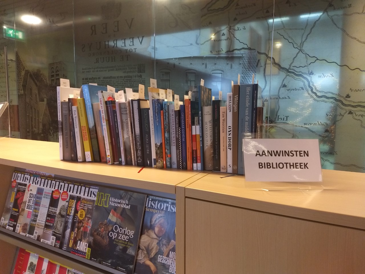 een rij boeken op een rijtje op een kast in de studiezaal met het bordje aanwinsten