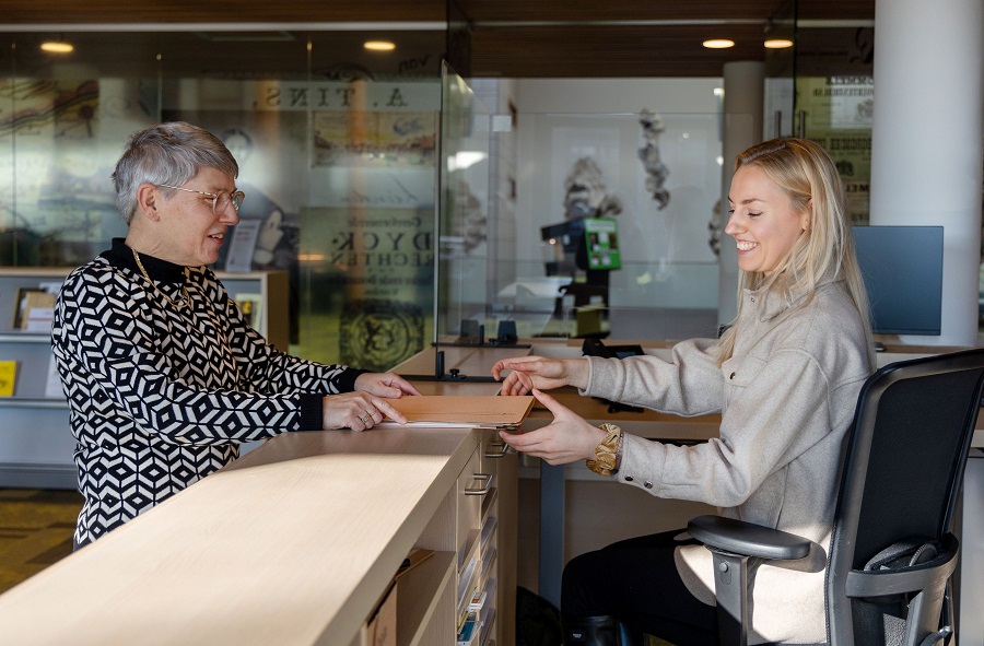Lotty overhandigt stukken uit depot aan studiezaalmedewerker Merel op de studiezaal van het Regionaal Archief Rivierenland